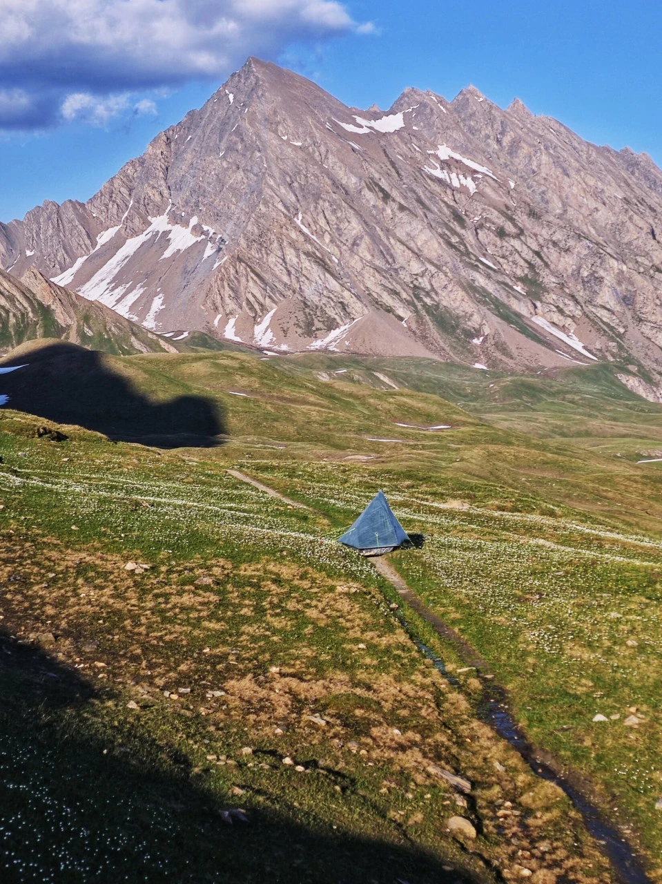 Tenda piantata su un alpeggio del TMB a inizio giugno, minuscola sotto la cima e la neve ancora presente: un'atmosfera che non esiste più una volta avviata l'alta stagione